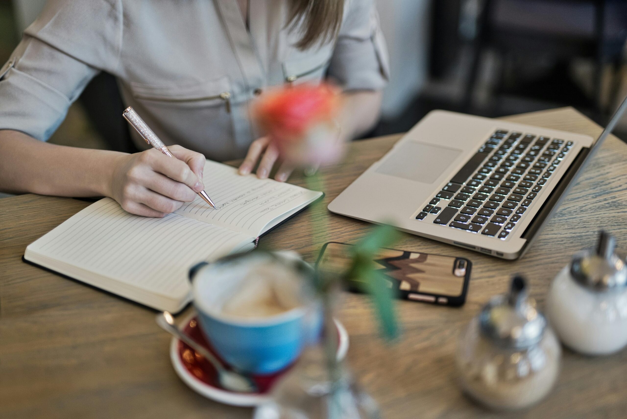 a lady writing content in her dairy in front of her laptop